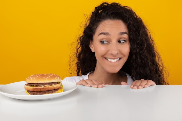 Hungrige Dame, die auf den Burger schaut, der aus dem Tisch lugt