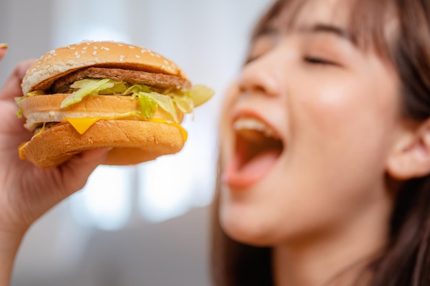 Hungrige junge Frau, die Junk-Food-Hamburger und Pizza zum Mittagessen isst, indem sie im Urlaub die Lieferung zu Hause bestellt. ungesunde Mahlzeit, Fettleibigkeitsrisiko.