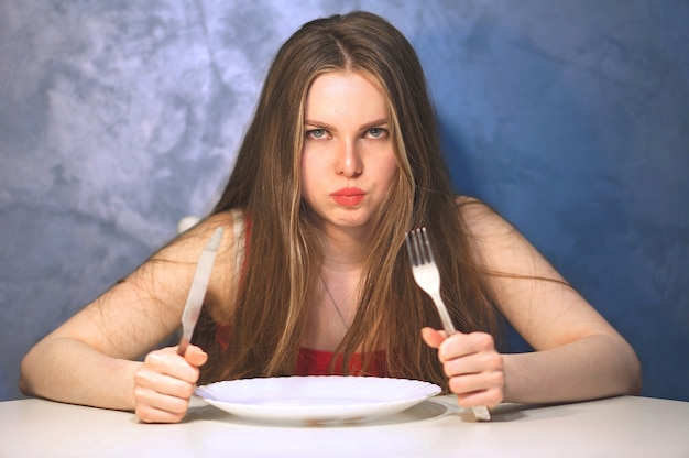 Hungrige junge Frau, die mit einem leeren Teller wartet