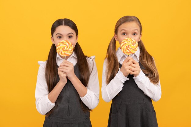 Hungrige Schulkinder halten bunte Strudellutscher auf Stöcken gelbem Hintergrund, Essen.