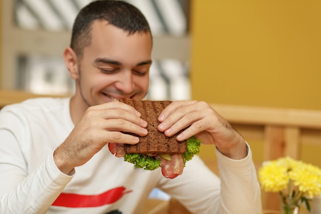 Hungriger junger mann im restaurant essen sandwich