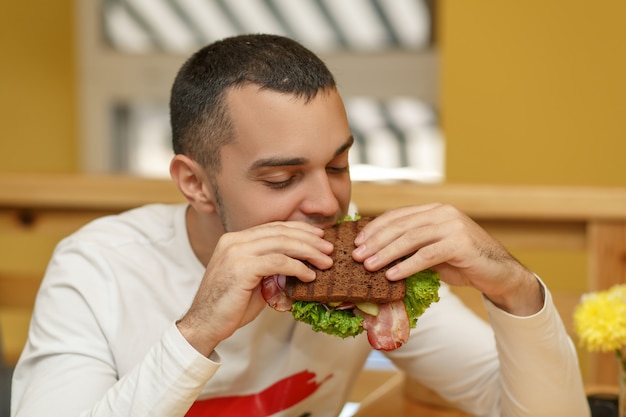 Hungriger junger mann im restaurant essen sandwich