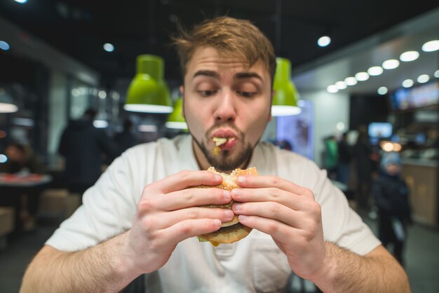 Foto hungriger mann mit bart isst gierig einen burger. lustiger mann, der ein sandwich betrachtet. konzentrieren sie sich auf den burger