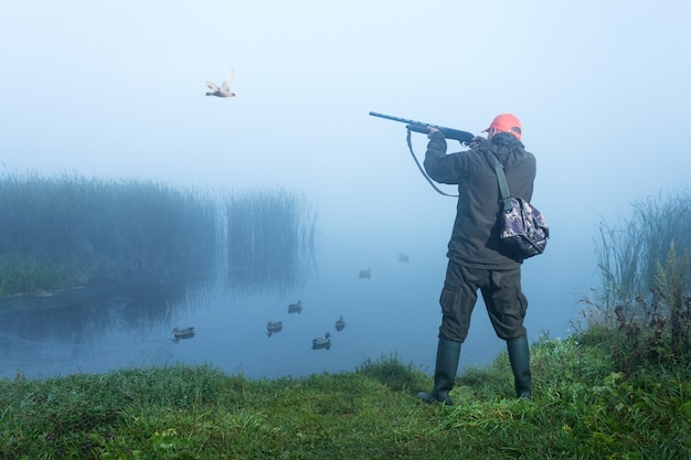 Hunter atirando no céu durante a caça ao pato na manhã de outono. Caça com isca de patos no lago.