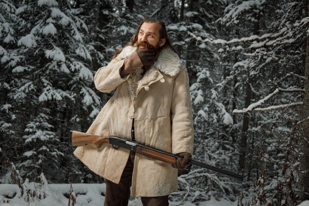 Hunter en ropa vintage de invierno con barba en el bosque con pistola