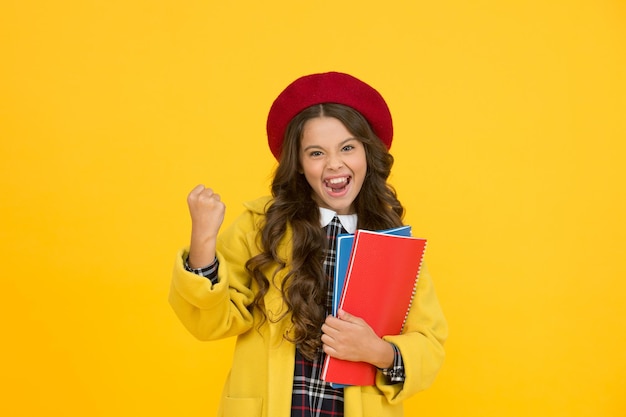Hurra. glückliches Kind in Schüleruniform. Kind in französischer Baskenmütze auf gelbem Hintergrund. stilvoller Teenager-Student. kleines Mädchen mit Notizbuch oder Arbeitsbuch für den Unterricht. Bildungskonzept. Schule und Mode.