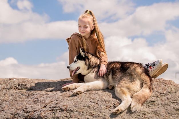 El husky siberiano y su bella amante de ojos azules están sentados en una roca contra el cielo El concepto de amor por los animales y la naturaleza