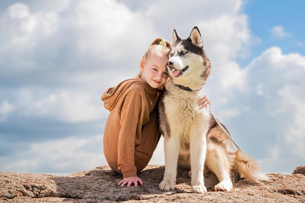 El husky siberiano y su bella amante de ojos azules están sentados en una roca contra el cielo El concepto de amor por los animales y la naturaleza