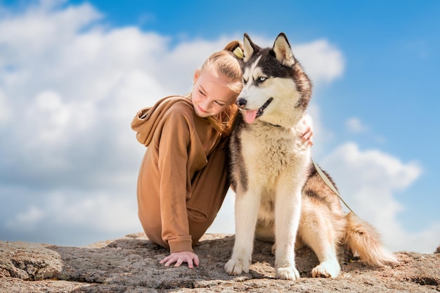 El husky siberiano y su bella amante de ojos azules están sentados en una roca contra el cielo El concepto de amor por los animales y la naturaleza