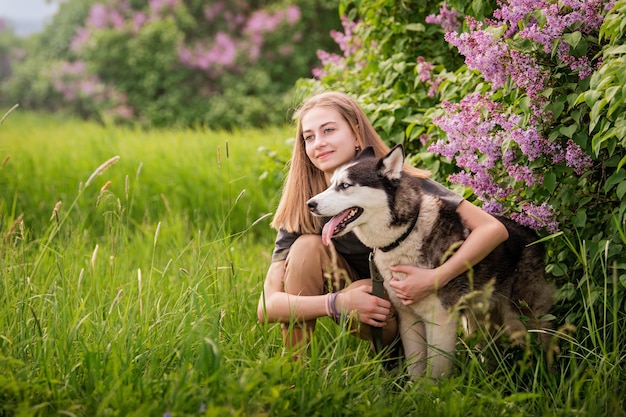 Un Husky siberiano y su hermoso dueño de ojos azules se abrazan mientras yacen en la hierba El concepto de amor por los animales y la naturaleza