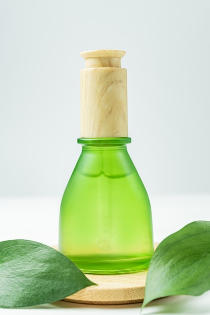 Hyaluronsäure-Ölmodell mit Kollagen und Peptiden in grüner Flasche auf Holzspiel mit grünen Blättern. Hautpflege Schönheitsprodukt flüssige kosmetische Serumverpackung. Konzept der organischen Wissenschaft