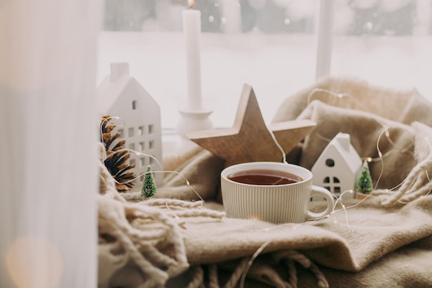 Hygge de inverno Xícara quente de velas de chá ilumina decorações de natal elegantes na janela Casa aconchegante