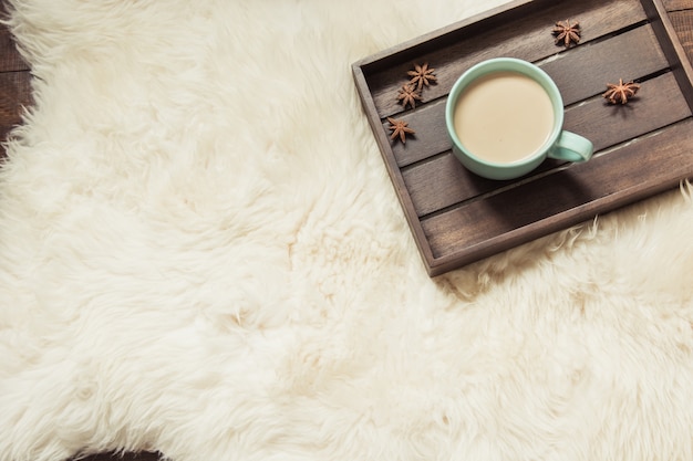 Hygge Stillleben mit heißer Tasse schwarzen Kaffee, warmem Schal auf Pelz und Holzbrett.