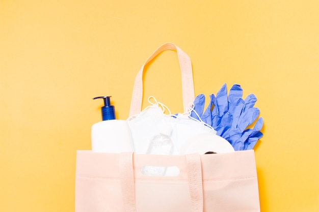 Hygieneprodukte in einer Stofftasche auf gelbem Grund, Schutzmasken, Flüssigseife, Toilettenpapier