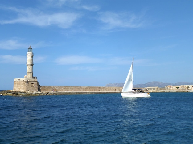 Iate de vela branca perto do farol no mar egeu azul, ilha de creta, grécia