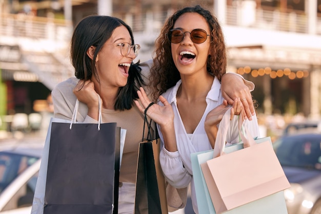 Ibamos a estar tan arruinados pero a quién le importa Foto de dos mujeres jóvenes y atractivas de pie afuera juntas y uniéndose mientras compran en la ciudad