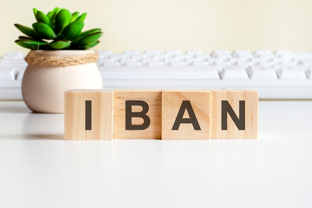 IBAN-Wort aus Holzklötzen. Vorderansicht-Konzepte, grüne Pflanze in einer Blumenvase und weiße Tastatur im Hintergrund. IBAN - Abkürzung für International Bank Account Number