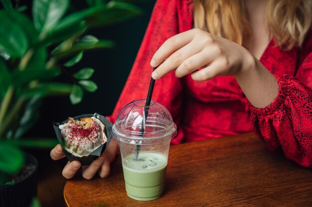 Ice matcha latte e cupcake closeup em um café nas mãos femininas