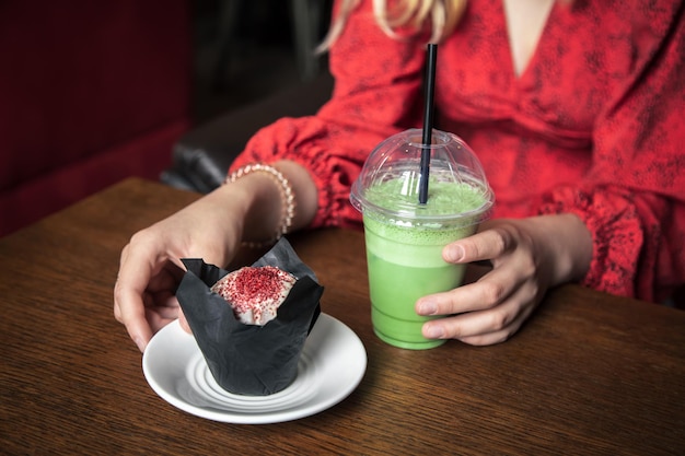 Ice Matcha Latte und Cupcake Nahaufnahme in einem Café in weiblichen Händen