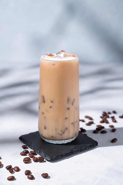 Foto iced coffee latte in einem hohen glas mit milch auf einem hellen hintergrund mit kaffeebohnen und morgenschatten sommer-erfrischungskonzept