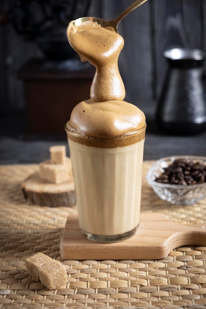 Iced dalgona coffee um café batido cremoso e fofo da moda em um fundo escuro de madeira com açúcar de moedor de café e grãos de café com colher de espuma