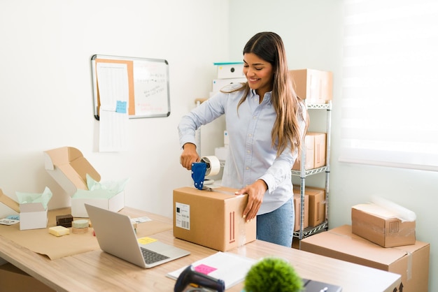 Ich bin zufrieden und stolz auf das Wachstum meines Unternehmens. Schöne Unternehmerin, die Klebeband auf ein Paket legt, das bereit ist, an einen Kunden versendet zu werden