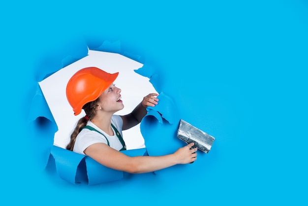 Ich brauche hilfe kind tragen helm auf der baustelle teenager-mädchen stuckateur mit werkzeugspachtel kind bei der reparatur des arbeitskonzepts der renovierung in der werkstatt beschäftigter professioneller zimmermann mit kelle