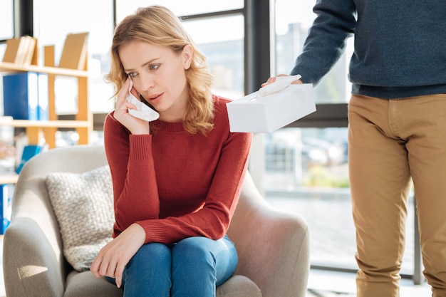 Ich fühle mich negativ. Unglückliche freudlose weinende Frau, die ein Papiertaschentuch hält und ihre Tränen wegwischt, während sie versucht, mit Emotionen umzugehen