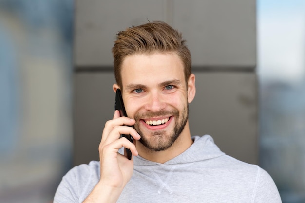 Ich habe auf deinen Anruf gewartet. Mannbart mit Smartphone, städtischer Hintergrund. Kommunikationskonzept. Mann mit Bart glücklich lächelndes Gesicht Gespräch Smartphone. Guy fröhlicher Anruf auf dem Smartphone.