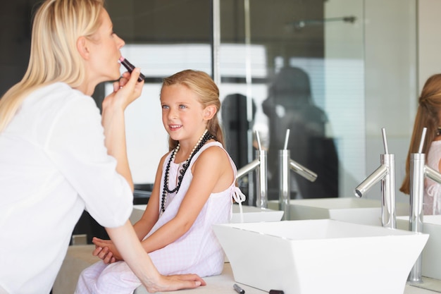 Ich kann es kaum erwarten, mein eigenes Make-up zu tragen. Kleines Mädchen sieht zu, wie ihre Mutter ihr Make-up aufträgt