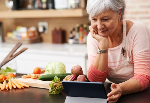 Foto ich liebe diese kochkanäle aufnahme einer frau, die ihr kinn auf ihre hände stützt, während sie ein tablet in ihrer küche betrachtet