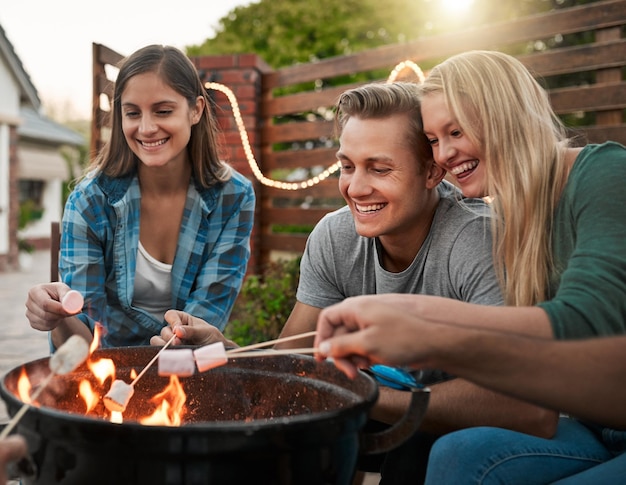 Ich liebe es, marshmallows um ein feuer herum zu rösten aufnahme einer gruppe fröhlicher junger freunde, die marshmallows auf stöcken über einem feuer draußen halten