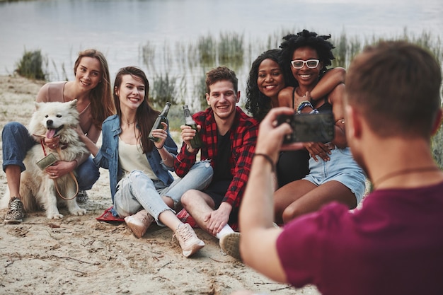 Ich mache gleich ein Foto von dir. Eine Gruppe von Menschen hat ein Picknick am Strand. Freunde haben Spaß am Wochenende.