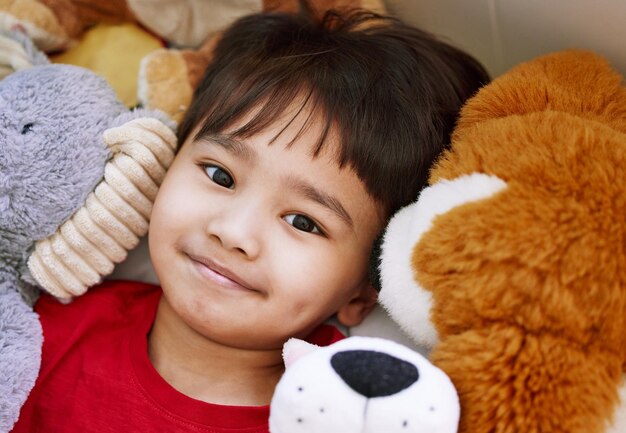 Ich mache immer ein Nickerchen mit all meinen Teddys Porträt eines entzückenden kleinen Jungen, der zu Hause mit seinen Stofftieren auf einem Bett liegt