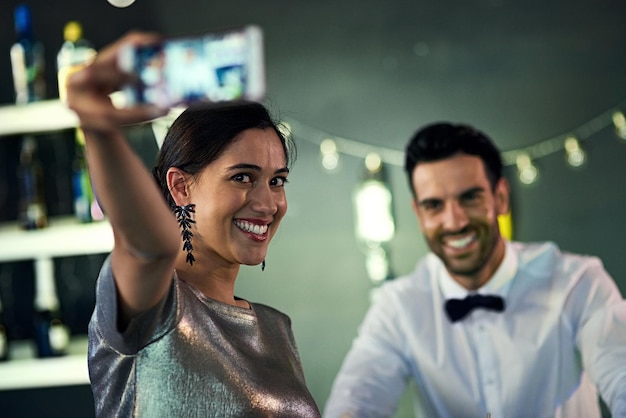 Ich möchte mich an diese Nacht erinnern Aufnahme einer jungen Frau, die mit dem Barkeeper in einem Nachtclub ein Selfie macht