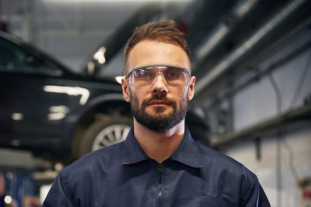 Ich schaue in die Kamera. Der Autoreparaturmann ist in der Garage mit dem Auto.