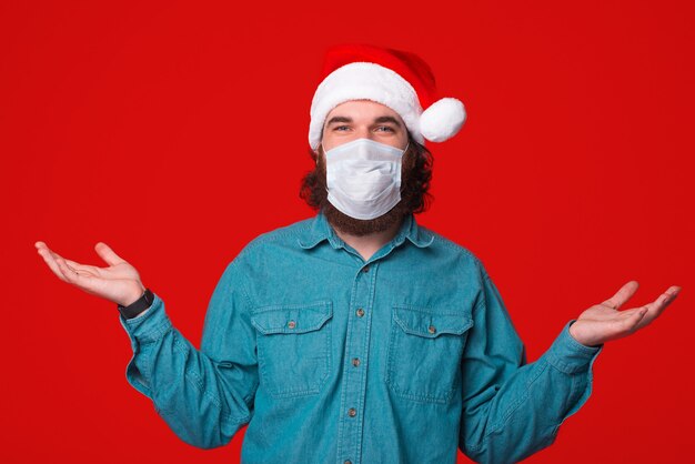 Ich weiß nicht, was ich tun soll, bärtiger Mann mit medizinischer Maske und Weihnachtsmannhut, Pandemiezeit