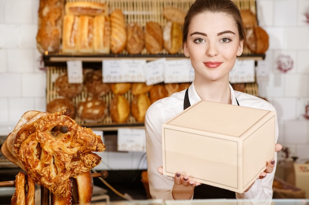 Ich weiß, was meine Kunden mögen. Schöne lächelnde Bäckerin, die eine Schachtel mit Bäckereidesserts heraushält