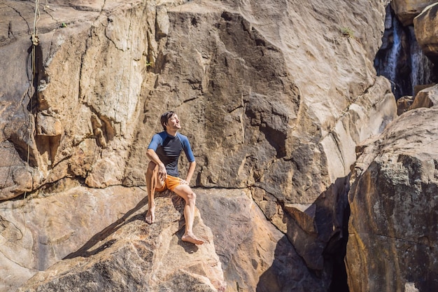 Ich würde für immer hier bleiben Schöner junger moderner Mann, der wegschaut, während er auf dem Felsen in der Nähe des Flusses sitzt