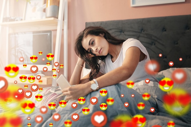 Ícones de mídia social em casa ou mulher tirando uma selfie para conteúdo ou post de namoro online no quarto Emojis de amor manhã ou garota relaxada no site de aplicativos móveis ou rede digital com emoticons de coração