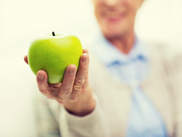 idade, alimentação saudável, comida, dieta e conceito de pessoas - close-up de mulher sênior sorridente feliz com maçã verde em casa