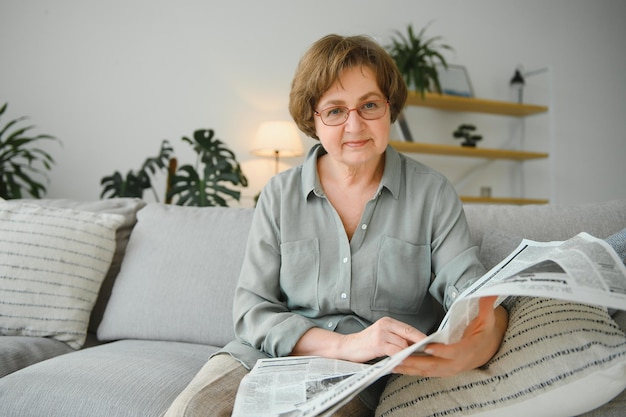 Idade e conceito de pessoas feliz mulher sênior lendo jornal em casa