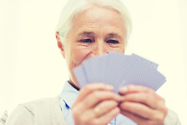 idade, jogo, jogo, poker e conceito de pessoas - close-up de mulher sênior sorridente feliz jogando cartas em casa