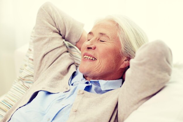 idade, relaxe e conceito de pessoas - mulher sênior sorridente feliz descansando no sofá e sonhando em casa