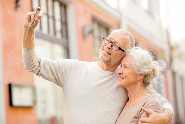 idade, turismo, viagens, tecnologia e conceito de pessoas - casal sênior com câmera tirando selfie na rua