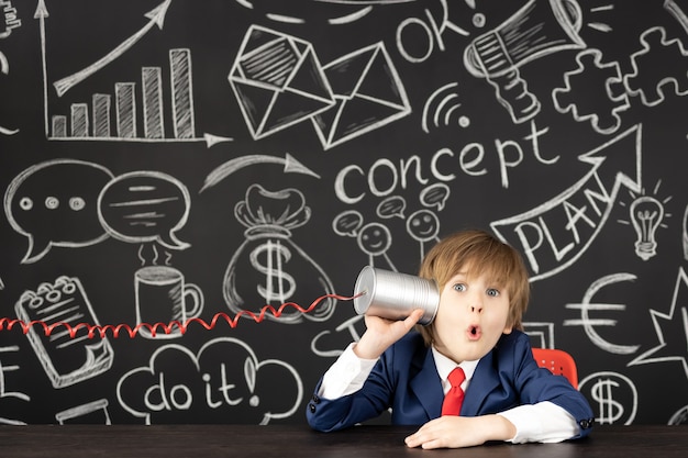 ¡Idea brillante! Estudiante niño divertido en clase contra la pizarra negra. Niño feliz finge ser empresario. Concepto de educación en línea y e-learning. De vuelta a la escuela