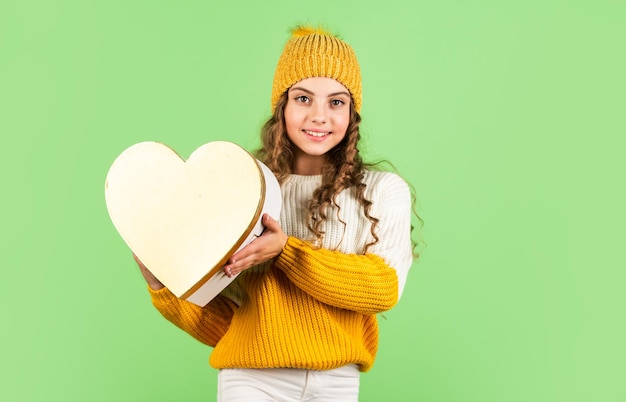 Idea de celebración de San Valentín Estado de ánimo romántico Tradición del día de San Valentín Sé mi San Valentín Felices vacaciones de invierno Niña alegre gorro de punto y suéter Niño sostenga el corazón caja de regalo fondo verde