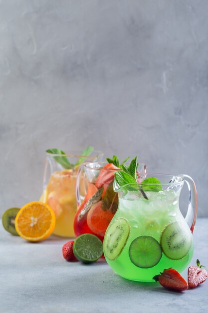 Idea creativa. Composición. Limonada de diferentes colores en jarras de vidrio con frutas y adornado con menta fresca y frutas en rodajas sobre la mesa.