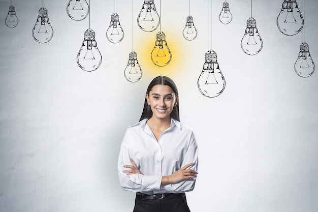 Idea creativa y concepto de puesta en marcha con una joven feliz y sonriente con camisa blanca en el fondo de la pared clara con bombillas blancas dibujadas a mano y una amarilla encendida