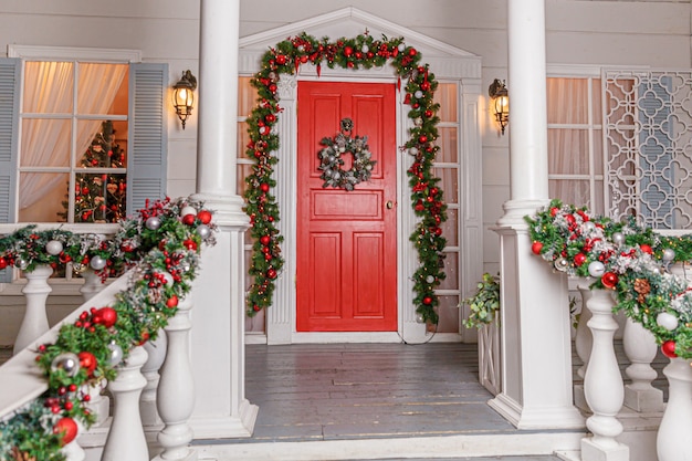 Idea de decoración de porche de Navidad. Entrada de la casa con puerta roja decorada para las vacaciones.